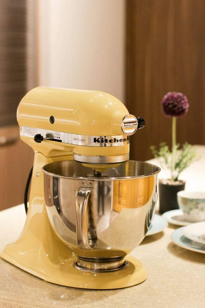 Vibrant yellow stand mixer on a kitchen countertop beside tableware and decor.